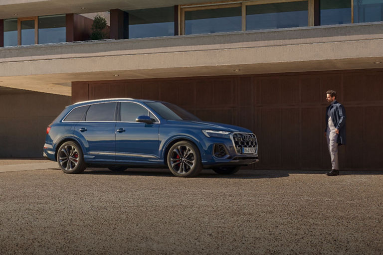 A blue SUV parked outside a modern building with a standing person nearby.