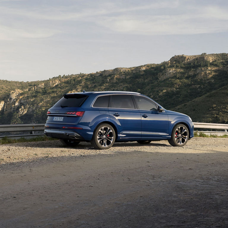 Audi SQ7 driving on a coastal road with a city skyline in the background.