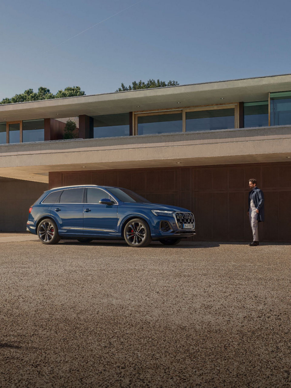 A blue SUV parked outside a modern building with a standing person nearby.