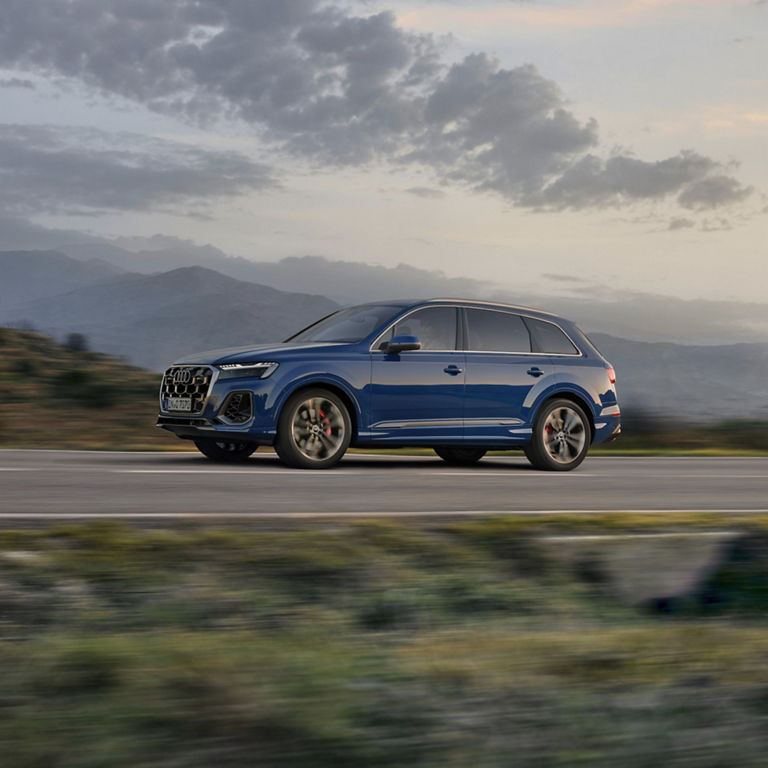 Blue SUV driving on a highway with mountains and cloudy sky in the background.