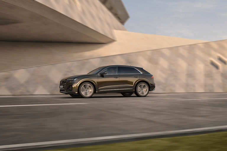 Audi Q8 tfsi e moving along road approaching modern bridge.