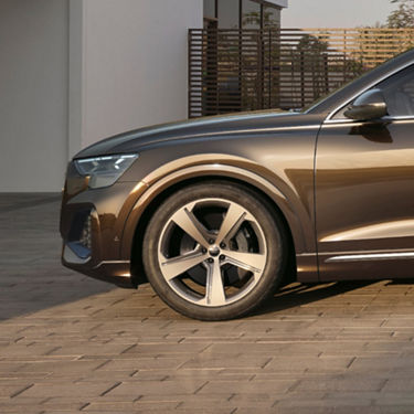  Front end of Audi Q8 tfsi e parked outside of contemporary built house.