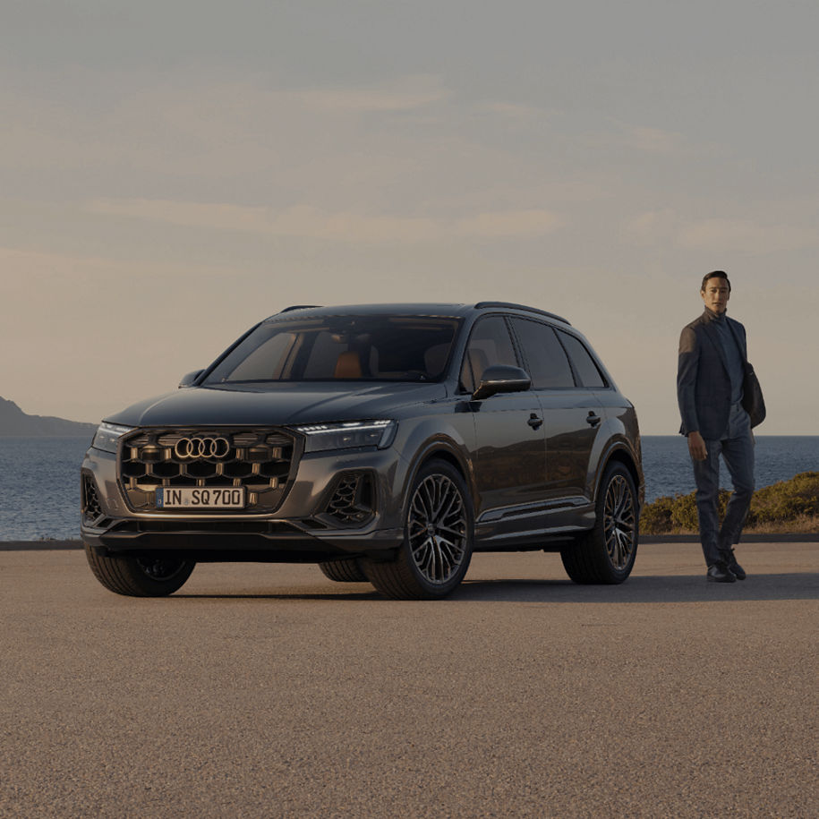 Audi Q7 SUV tfsi e with man standing near rear end with coastal background.