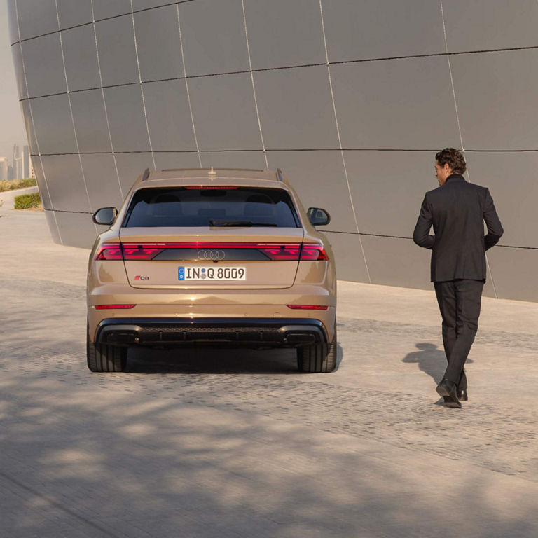 A man walking towards an Audi Q8 SUV parked near a modern designed wall.