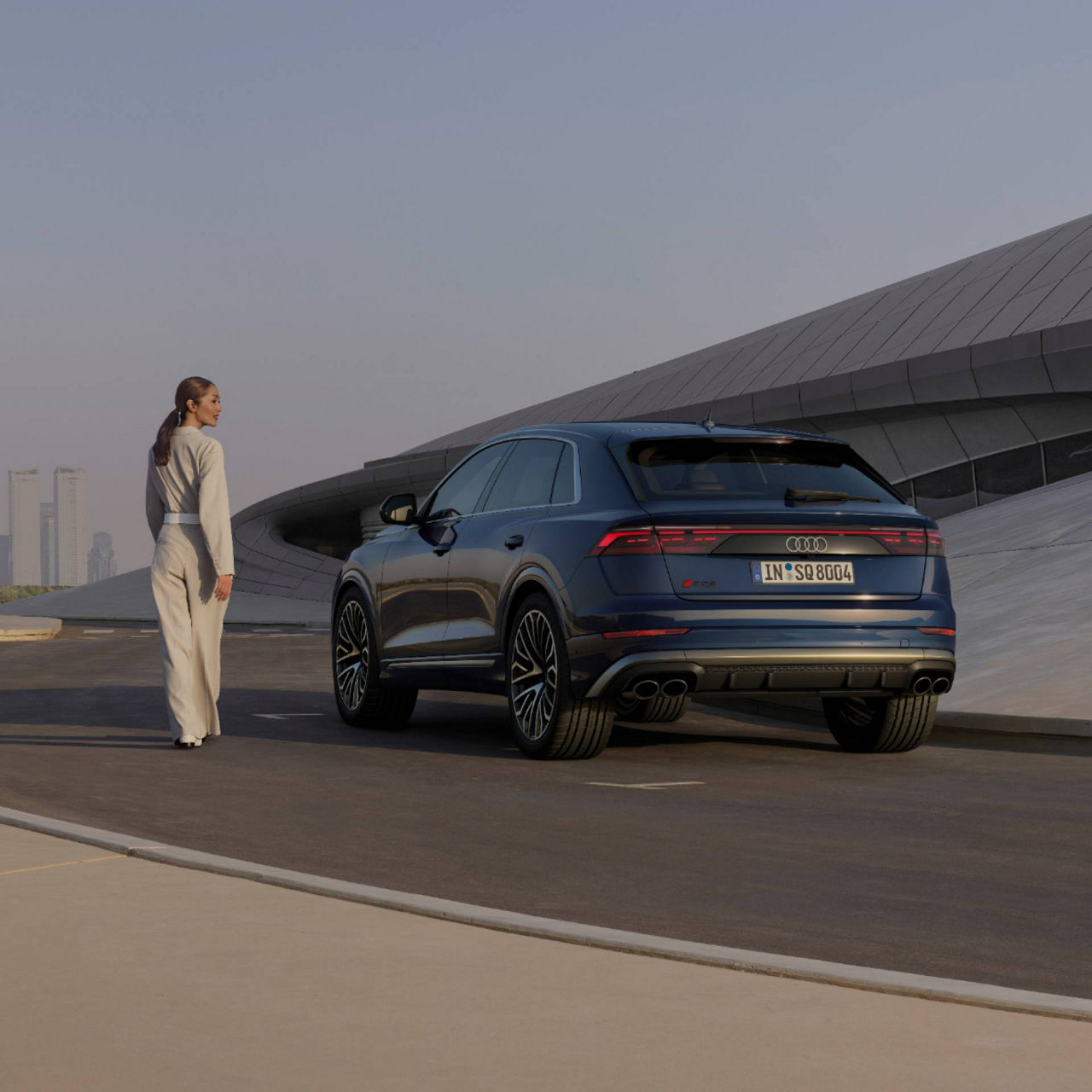 Lady standing aside blue Audi Q8 SUV in front of modern building.