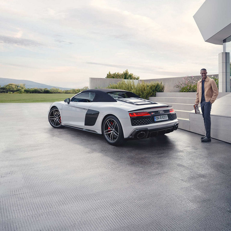 A white metallic Audi R8 convertible parked outside a modern building.
