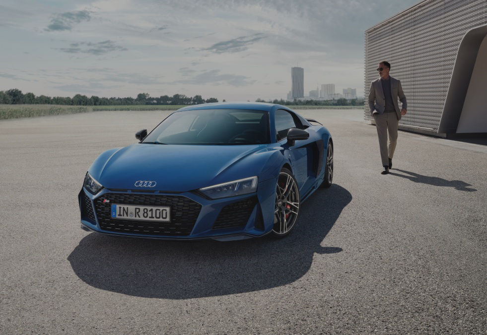 A blue Audi R8 parked with a man in a suit walking towards it.