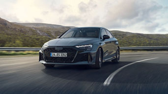 A grey Audi RS 3 Saloon driving on a mountain road with a blurred scenery