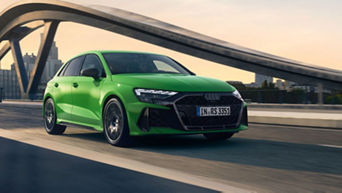 A green Audi driving on a bridge with an urban skyline in the background.