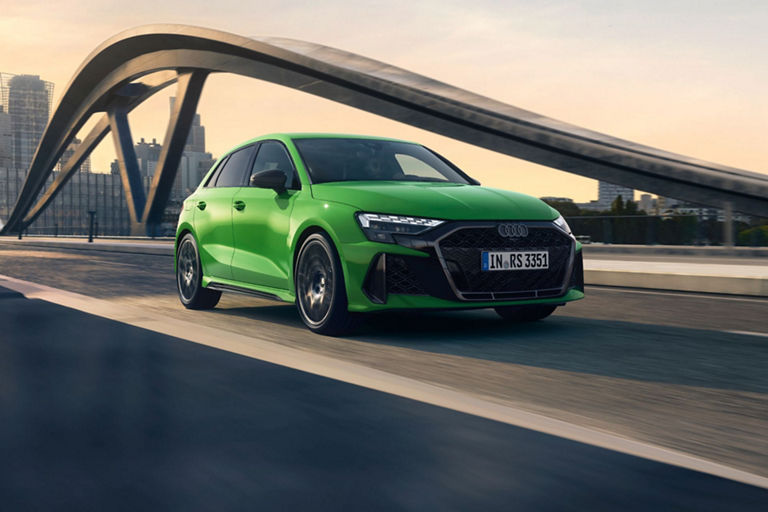 Green Audi RS3 Sportback driving on a bridge with city skyline in the background.