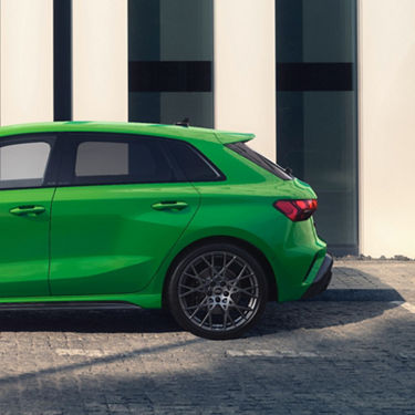 Bright green Audi RS3 car parked beside glass building.