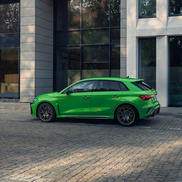 Bright green Audi RS3 Sportabck car parked beside glass-fronted building.