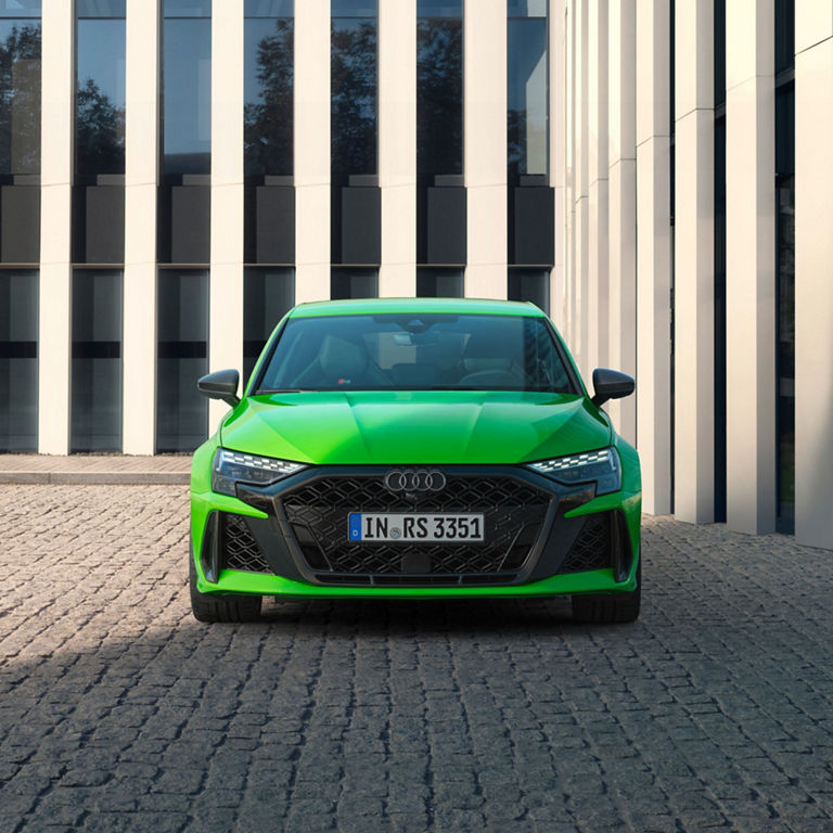 Bright green Audi RS3 Sportback parked in front of a modern building.