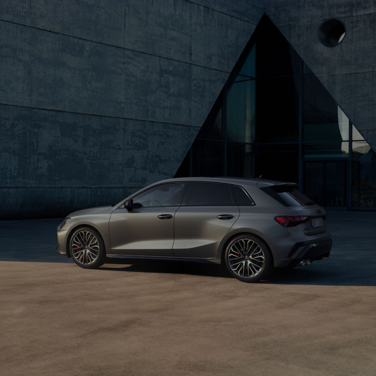 Audi RS3 Sportback car parked by a modern concrete building with a triangular glass entrance.