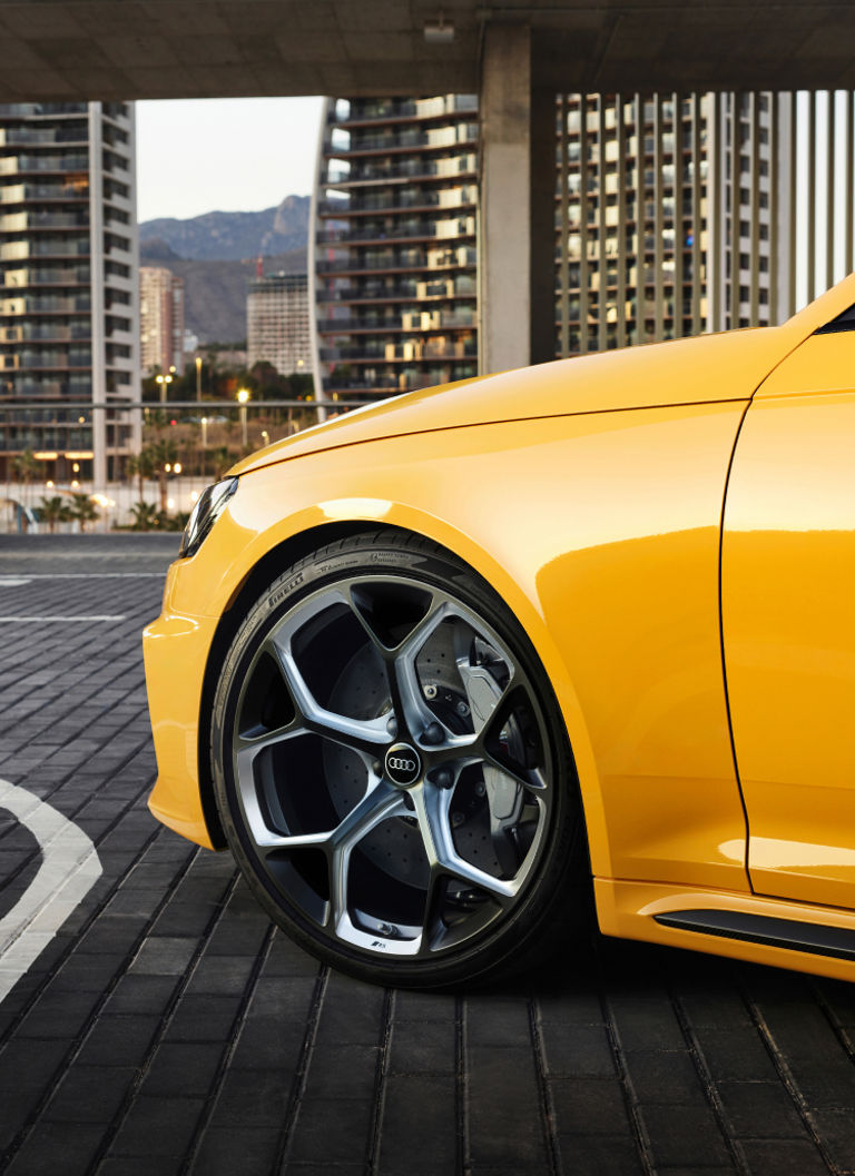 Close-up of a yellow car's front wheel and fender, parked in an urban area.