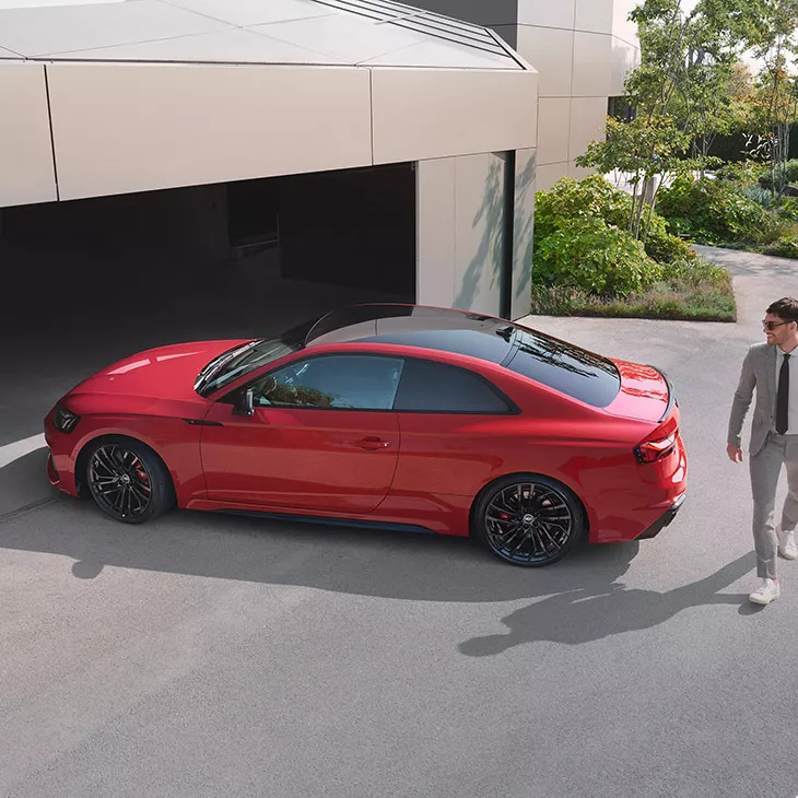 A red car parked outside a modern building, with a person approaching.