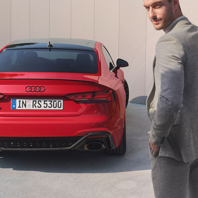 Red Audi RS5 Coupe parked next to a man in a grey suit.