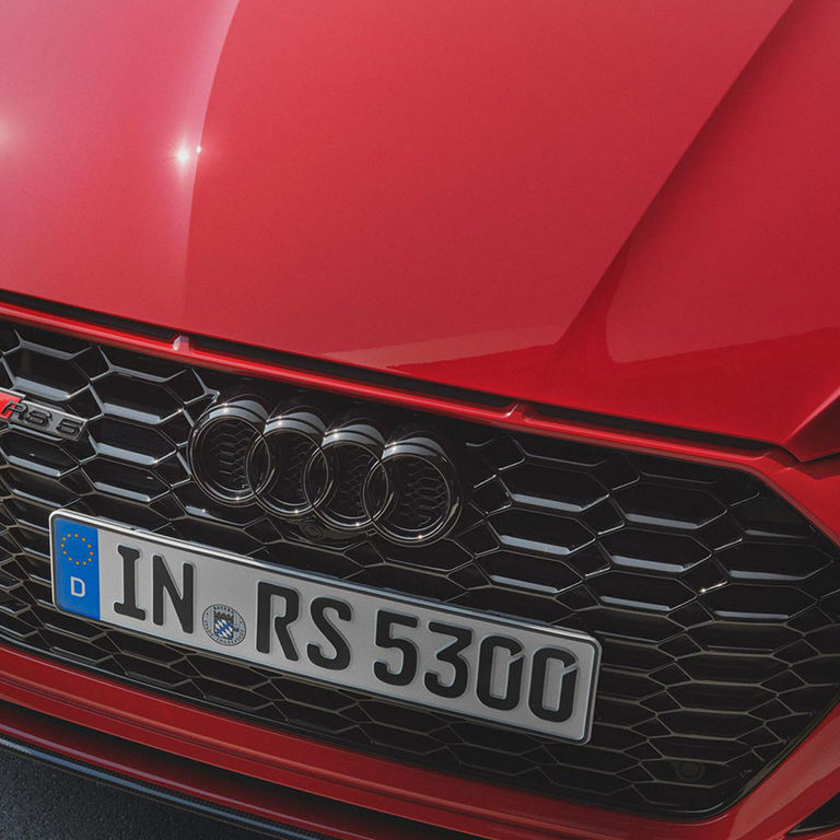 Close-up of a red car's grille with the Audi logo and a European license plate reading "IN RS 5300".