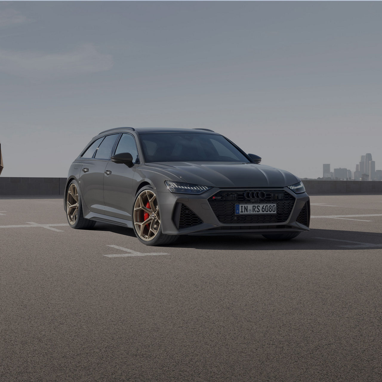 A grey Audi RS 6 Performance parked on an empty lot with a city skyline in the background.