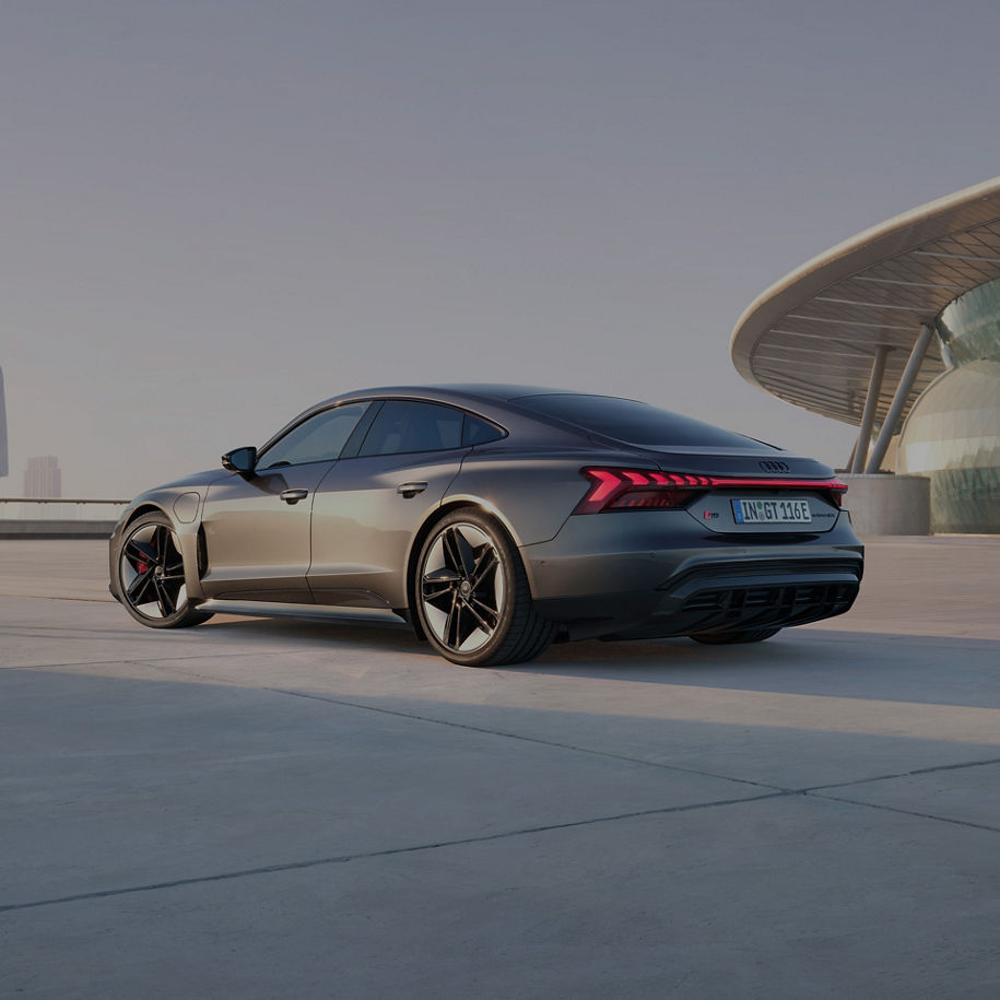 A grey Audi RS e-tron GT parked outdoors at dusk with modern architecture in the background.