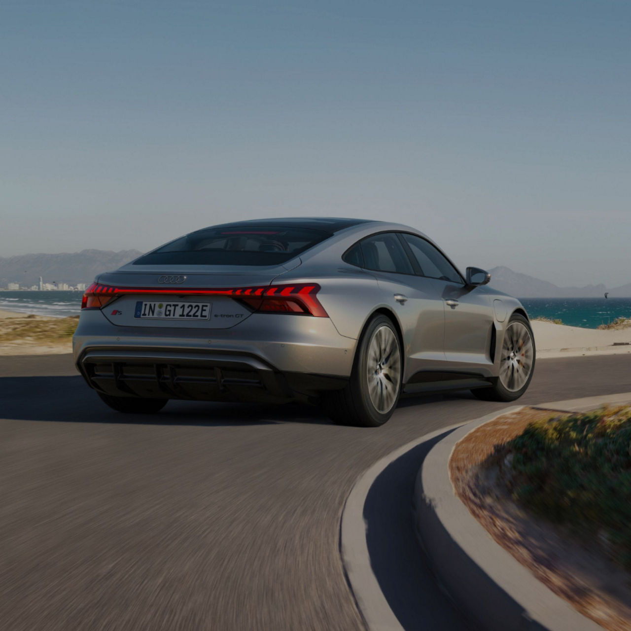 Silver Audi S e-tron GT driving on coastal road with clear skies.