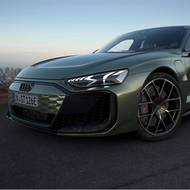 A green Audi electric vehicle with sleek headlights, parked with a blurred cityscape in the background.
