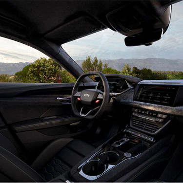 Interior view of a Audi car with steering wheel, dashboard, and mountainous landscape visible through windshield.