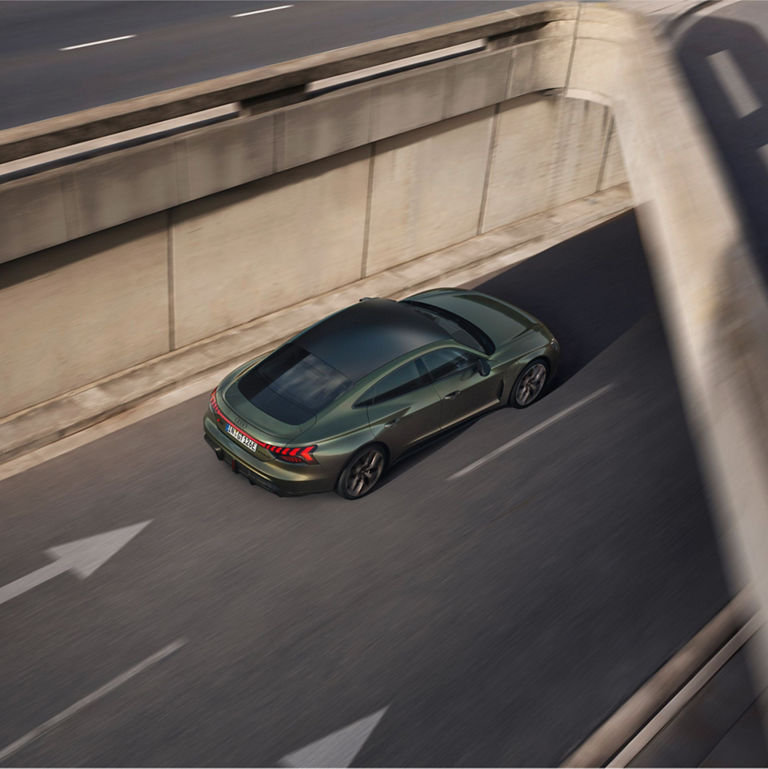 Aerial view of a green sedan driving on a road with concrete barriers on the side.