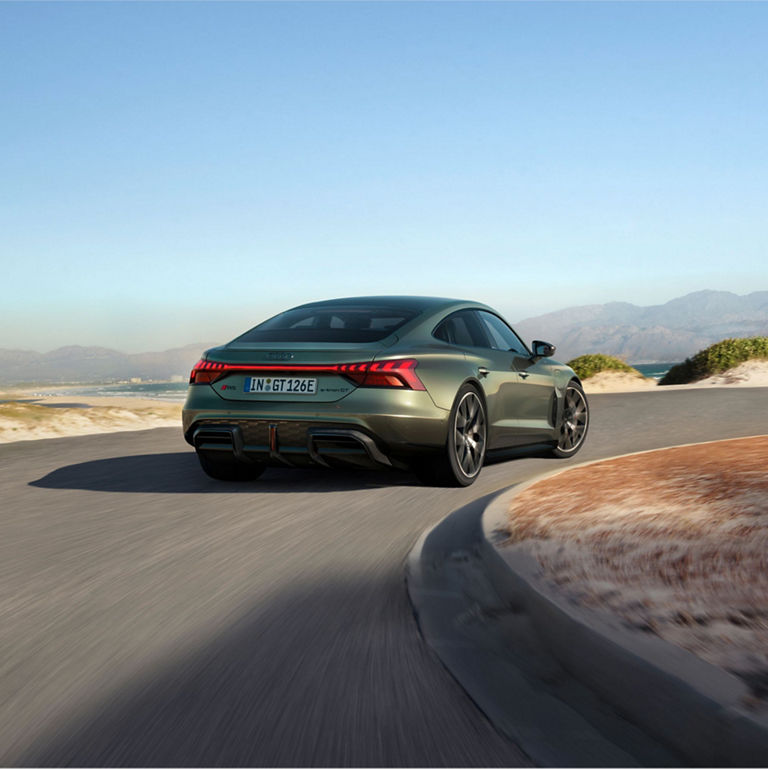 Green Audi RS e-tron GT Performance car on coastal road with mountains in the background.