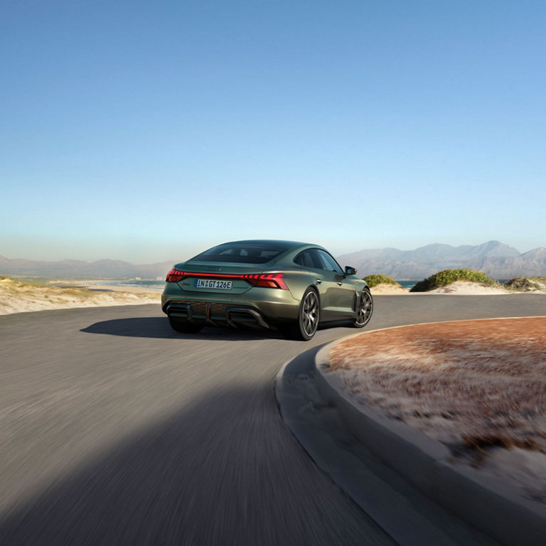 A green sedan driving on a coastal road with mountains in the background.