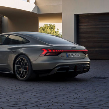 Rear view of a silver Audi RS e-tron GT parked outside a modern home.
