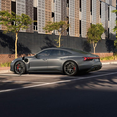 Audi RS e-tron GT parked on a street with charging on, modern building facade in the background.