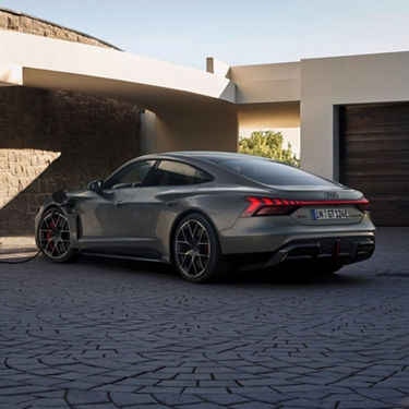 A grey Audi RS e-tron GT parked and charging outside a modern house.