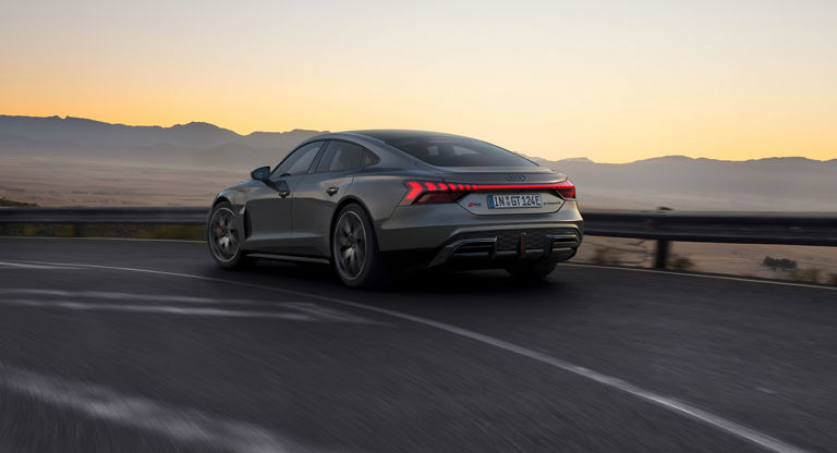 Grey Audi RS e-tron GT driving on highway at dusk with mountainous backdrop.