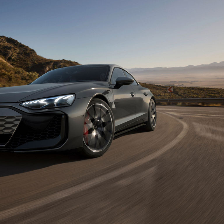 A grey Audi driving on a highway with mountainous scenery in the background.