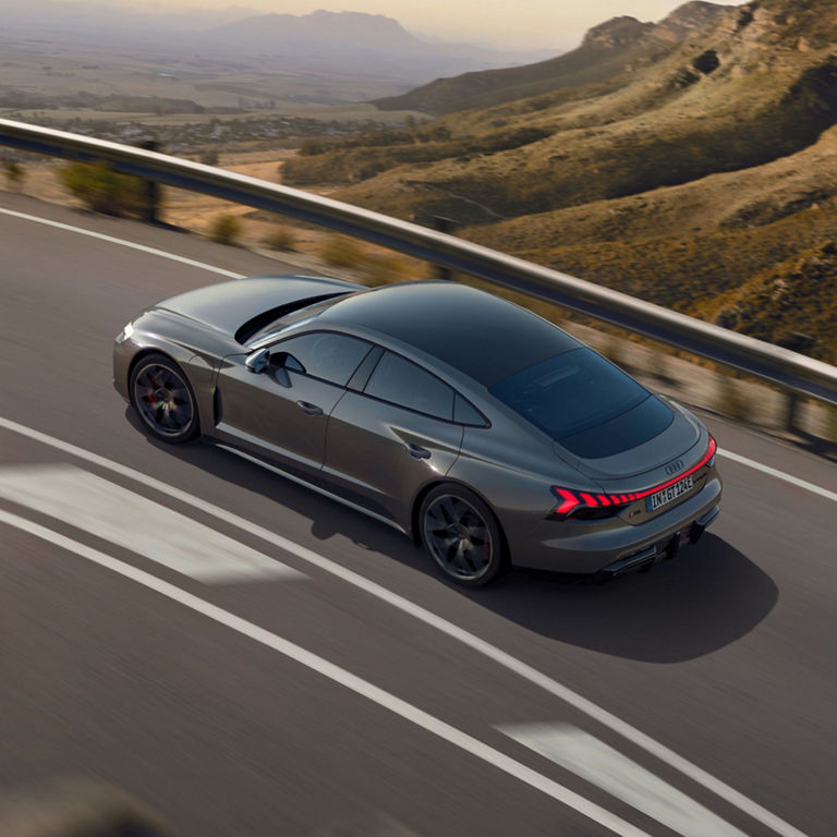 A grey Audi driving on a highway with mountainous scenery in the background.