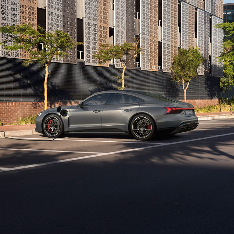 A grey sedan parked beside a charging station on an urban street.