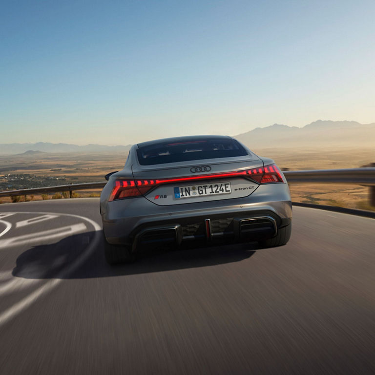 A grey Audi RS e-tron GT driving on a mountain road with a scenic backdrop.