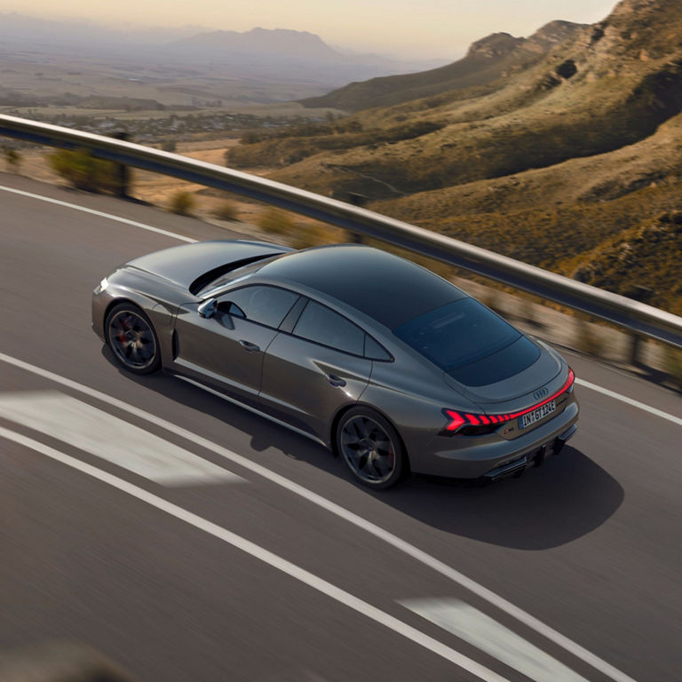 A sleek grey sports car driving on a mountainous road with a scenic backdrop.