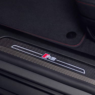 Close-up of a car's door sill with carbon fiber texture and illuminated "RS" logo.