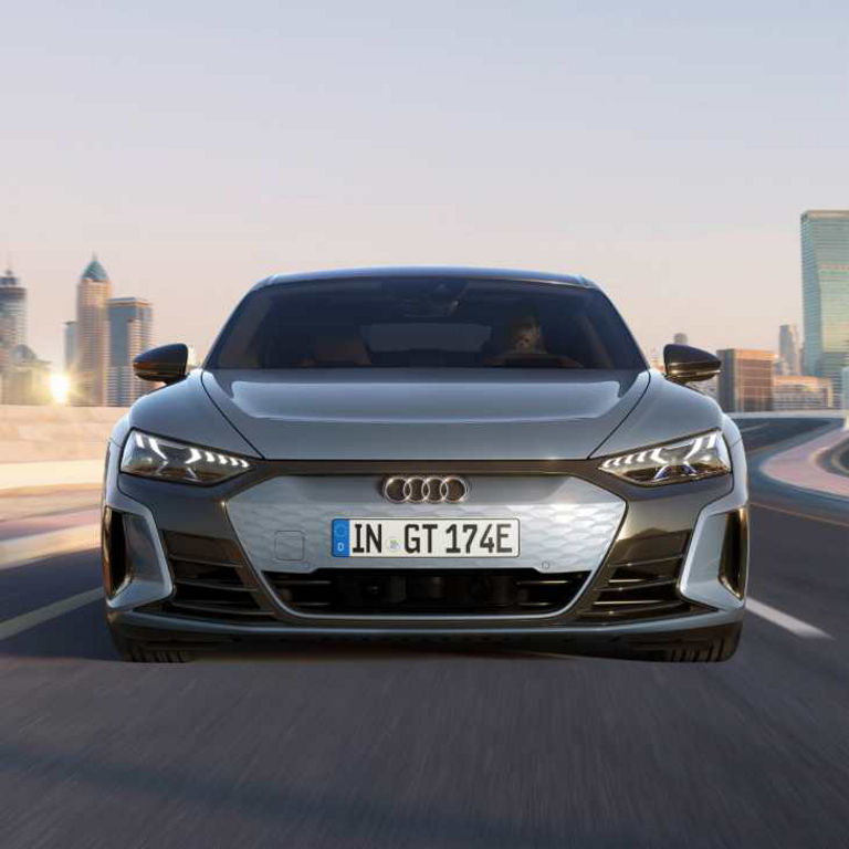 Audi electric car driving on a highway with a city skyline in the background.