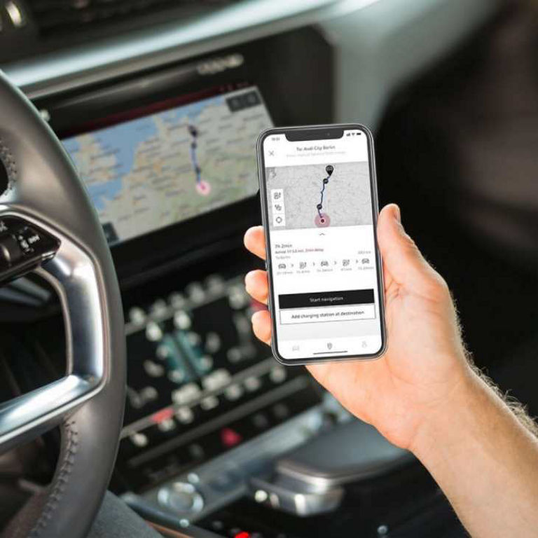 Person holding smartphone with map app inside a car, with vehicle's steering wheel and dashboard visible.