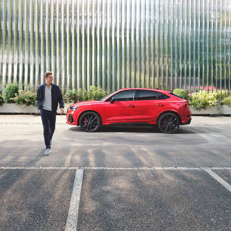Red car parked in front of a modern building with reflective glass facade.