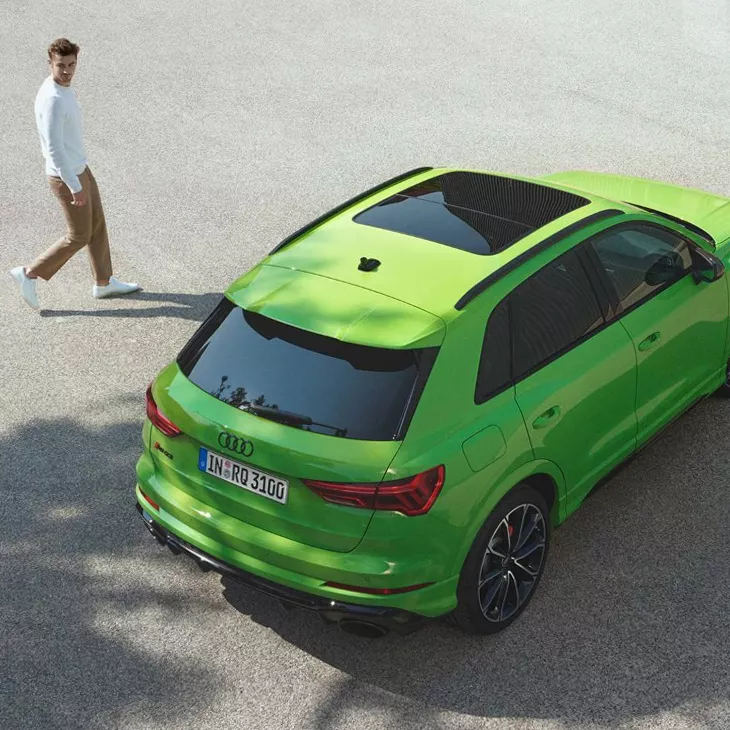 Ariel view of man approaching green Audi Q3 on open space tarmac.