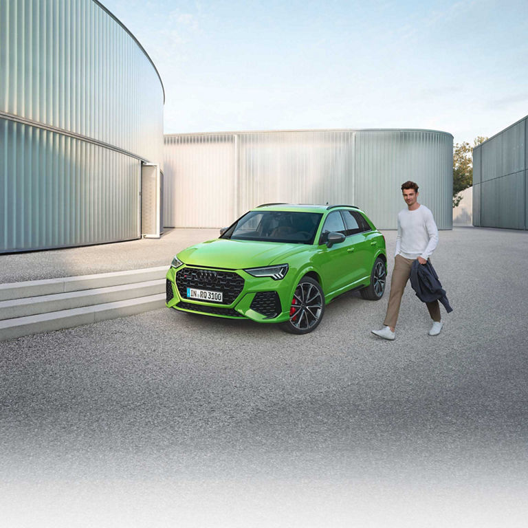 Man walking past green Audi RS Q3 parked outside a modern building.