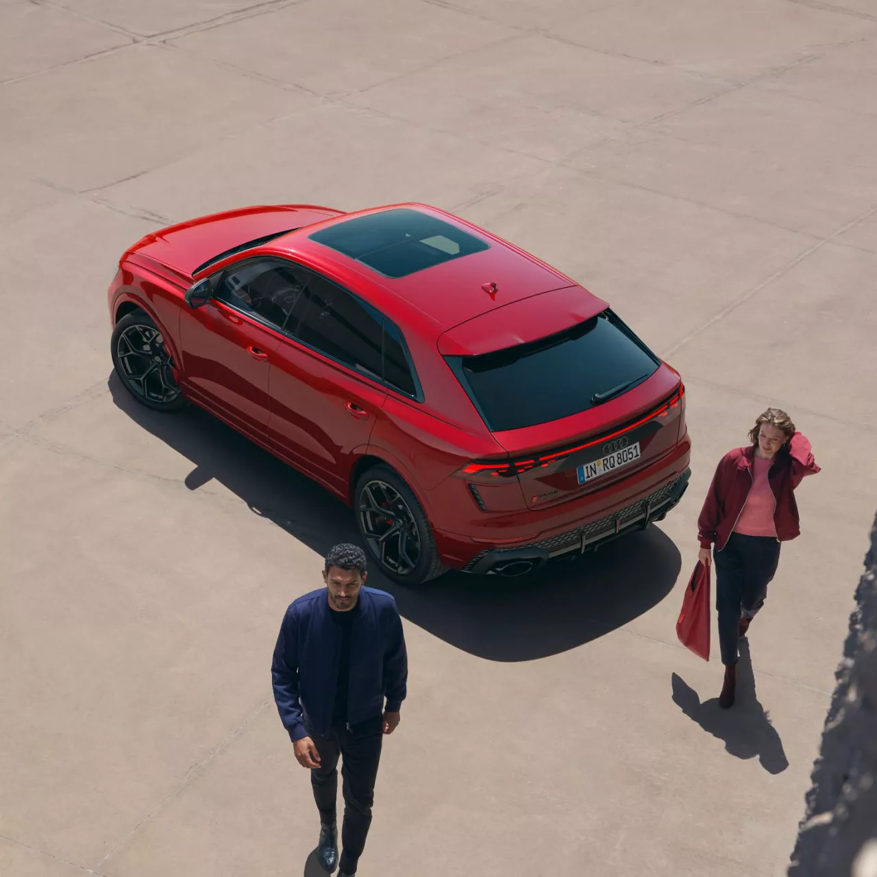 Red SUV parked on concrete with two people walking nearby.