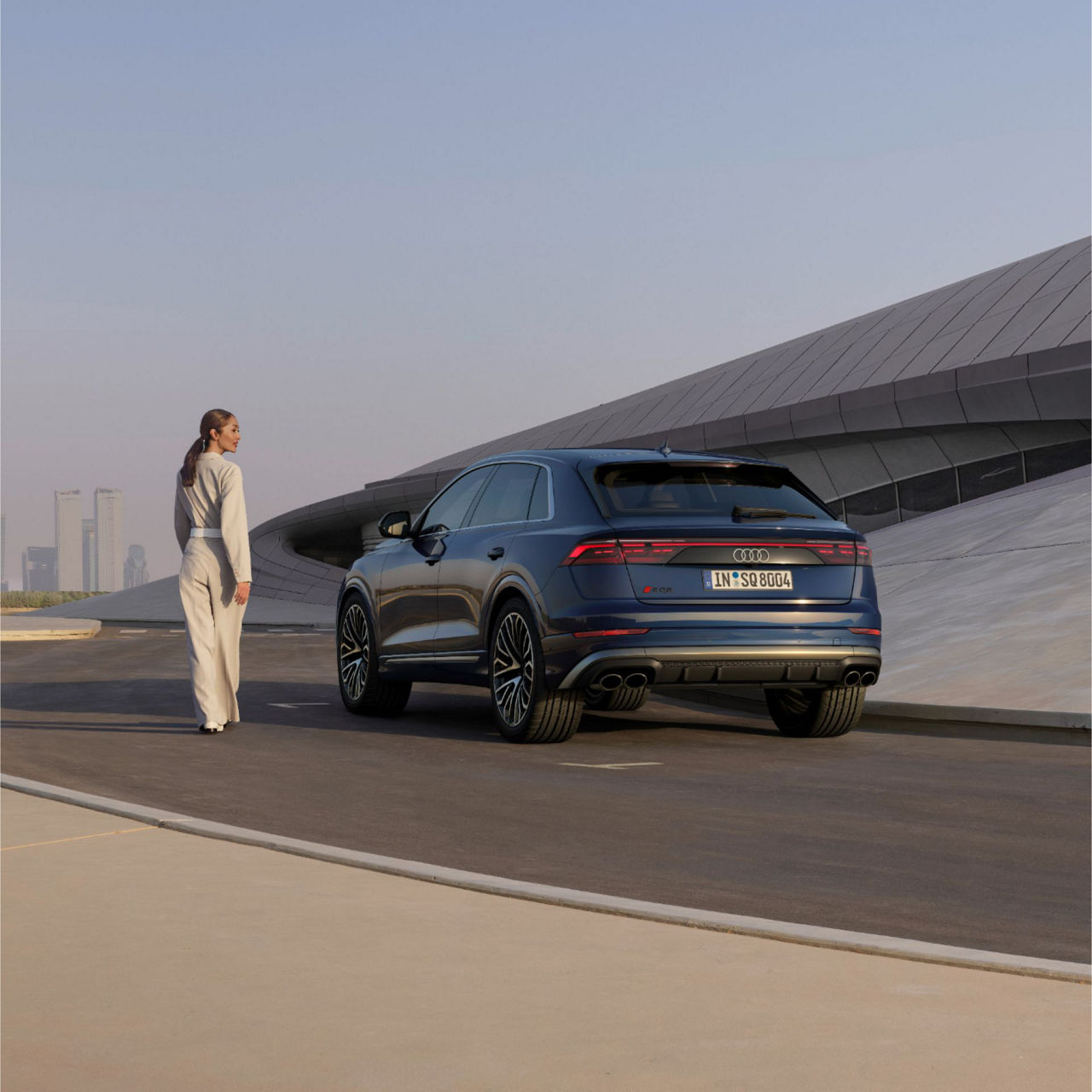 Lady walking away standing next to Audi RS Q8 with urban skyline in the background.