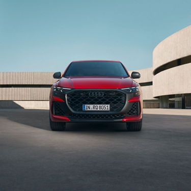 Front view of a Red Audi RS Q8 Performance with a modern building in the background.