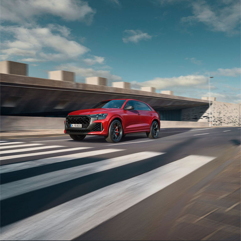 Red Audi RS Q8 Performance moving at speed approaching a zebra crossing.