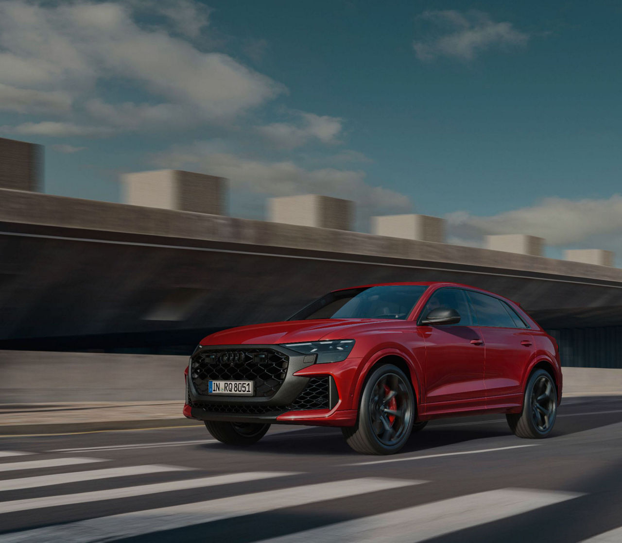 Red Audi RS Q8 approaching zebra crossing with blurred background.